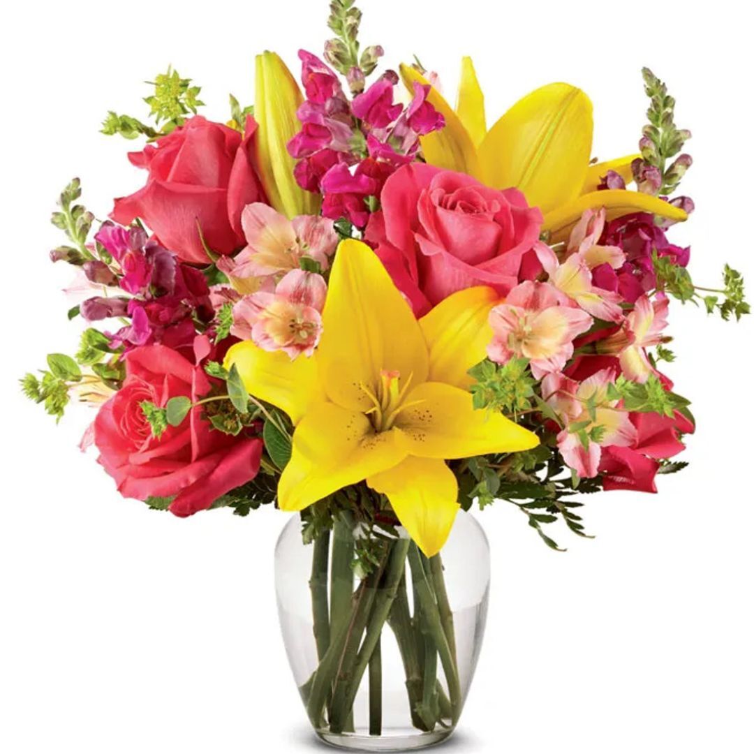 Vibrant bouquet featuring yellow lilies, pink roses, and assorted blooms arranged in a glass vase, isolated on a white backdrop.