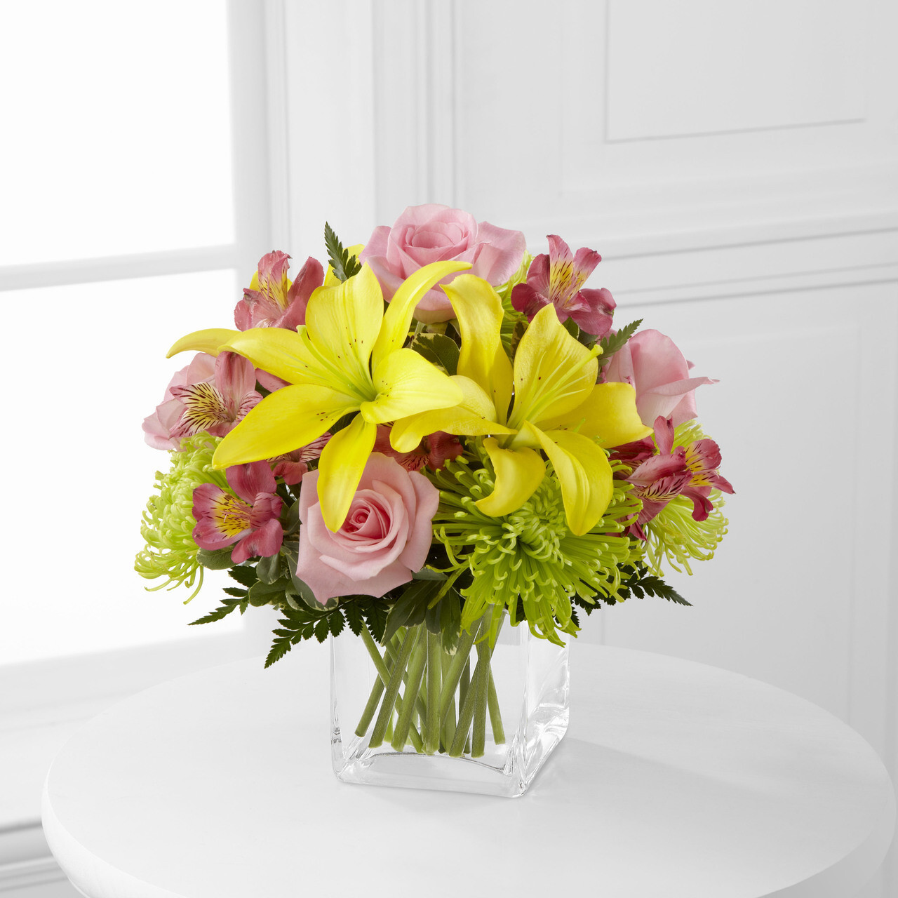 Vibrant bouquet featuring yellow lilies, pink roses, and green chrysanthemums in a clear glass vase