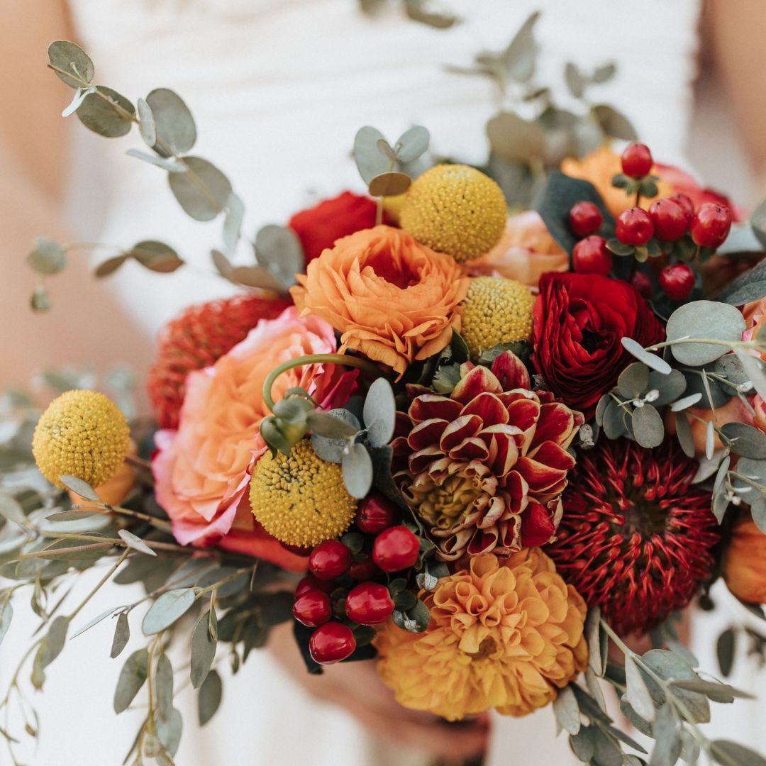 Close-up of an autumn-inspired bouquet featuring roses, dahlias, billy balls, and greenery in warm tones.