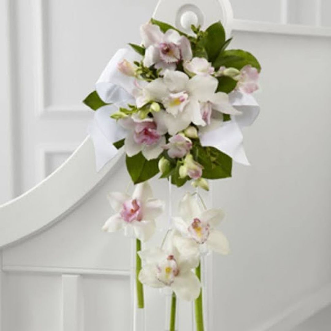Elegant floral decoration of orchids and greenery tied with a white ribbon, displayed on a white wooden chair.