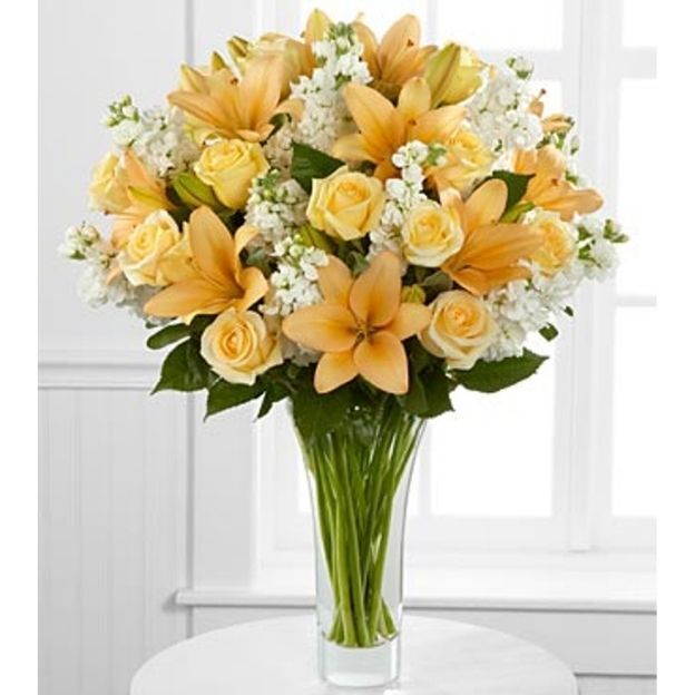 Elegant floral arrangement with pastel lilies and roses in a glass vase, set in front of a window.