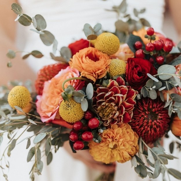 Warm seasonal floral arrangement featuring orange, red, and yellow blooms with greenery and berries.