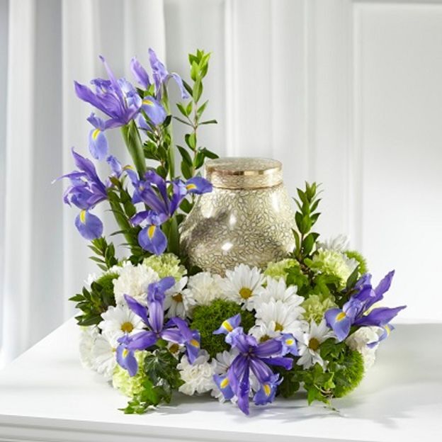 Memorial arrangement: vibrant purple irises, white daisies, and green button mums encircle a patterned gold urn.