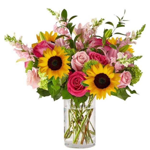 Bright yellow sunflowers with hot pink and blush roses, green accents, and stems showing in a cylindrical vase.