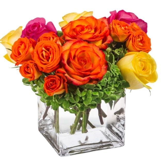 Vibrant rose arrangement in a cube vase featuring fiery orange, magenta, and yellow blooms with lush green accents.