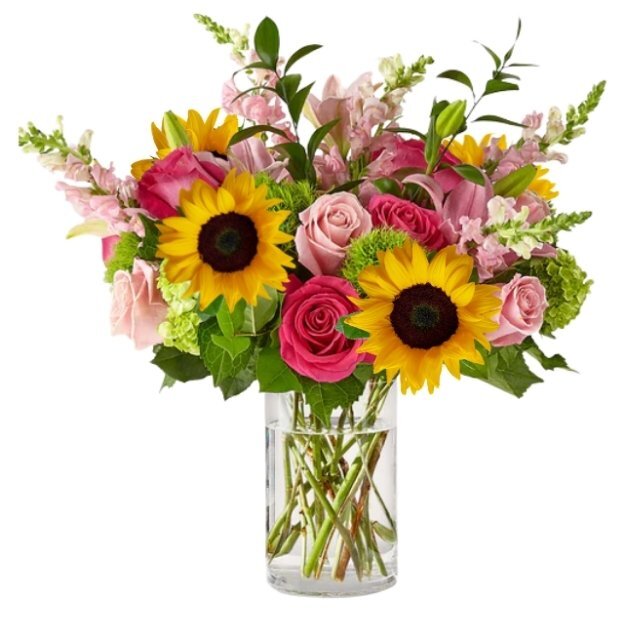 Bright floral arrangement featuring sunflowers, pink and hot pink roses, and greenery in a clear glass vase.