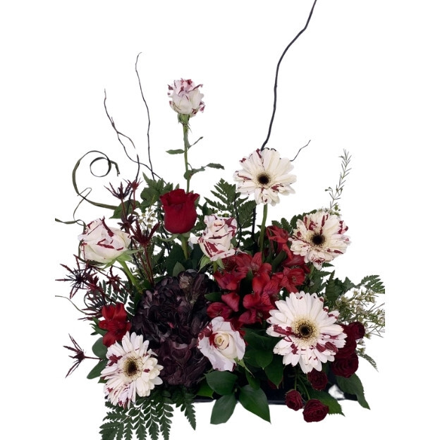 Dramatic floral arrangement with burgundy blooms, red roses, white flowers, fern leaves, and curling branches.